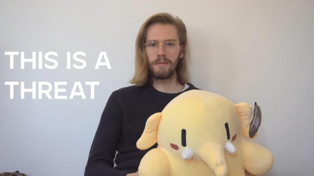 A screenshot from the video showing a mastodon plushie sitting on Erik Uden's lap with text next to him saying “this is a threat”