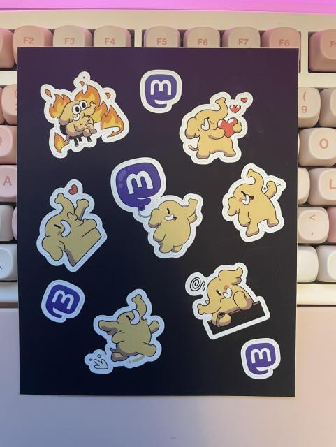 A sheet of stickers featuring the Mastodon creature in various situations, laying on top of a keyboard.