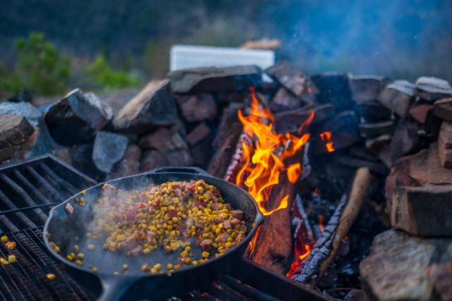 Food in a cast-iron pans sits over a campfire. [Fuji X-T5 / Fuji 23 1.4]
