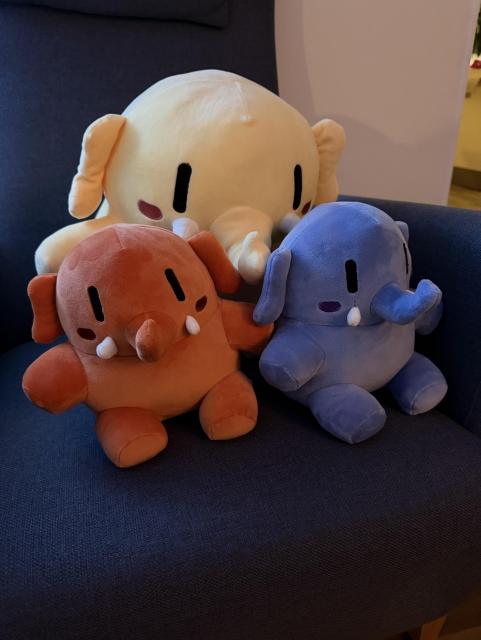 One big and two small Mastodons (plushtodon) sitting in a chair. 