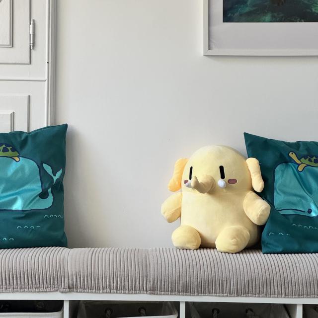 Plushtodon sitting on a couch between two pillows