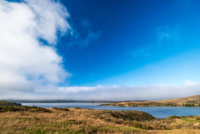 Under wide blue skies, grassy hillsides surround a little body of water. [Fuji X-T5 / Fuji 10-24 WR]