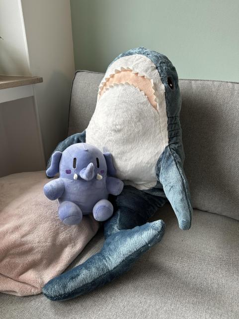 La peluche de mastodon installée sur le canapé avec un grand blahaj (requin en peluche ikea) 
