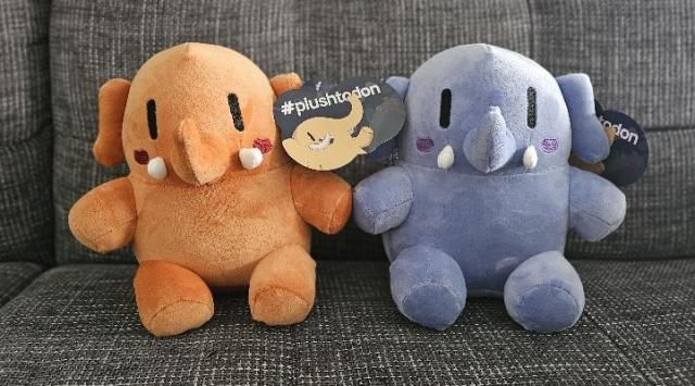 Two plushtodons are sitting on a couch.