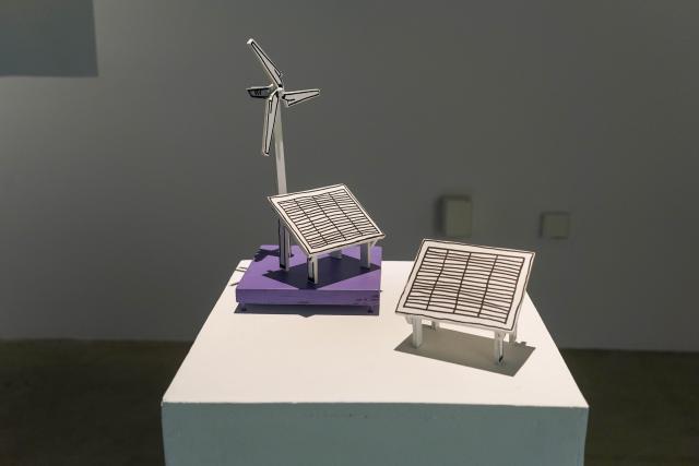 White plinth on which are placed small DIY maquettes of solar panels and an wind turbine