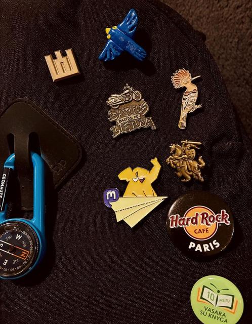 Assorted pins on a backpack: Lithuanian coat of arms, handmade Ukrainian freedom bird, Mastodon enamel pin, Eurasian hoopoe bird, logo of a biker friend, Hard Rock cafe Paris, etc