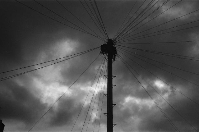 A power pole connecting many power lines, in front of a dramatic, cloudy sky.