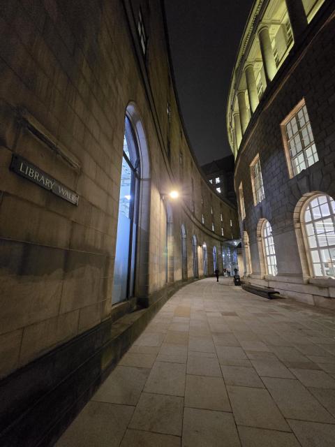 night photo of a curved alley between buildings in Manchester with a sign on the wall with text "library walk"