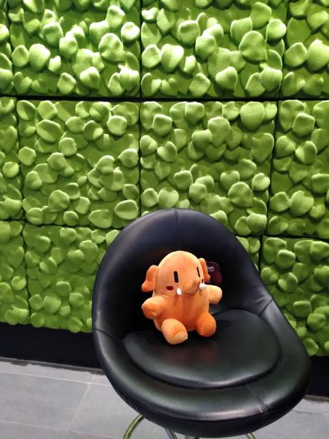 Plushtodon sitting on a chair, background being a funky greenish wall.