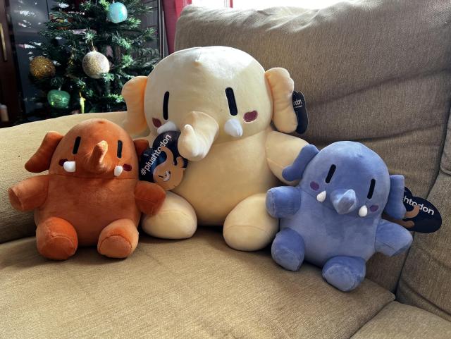 Una foto del peluche de Mastodon y sus dos versiones mini sobre un sofá con un árbol de Navidad de fondo.