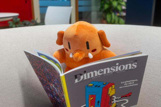 Plushtodon, assis dans un canapé, et lisant le numéro 19 du magazine de l'EPFL «Dimensions»