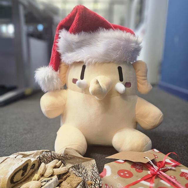Das Mastodon-Mastkottchen hat eine Nikolaus-Mütze an und sitzt vor einem Teller mit Plätzchen und einem Weihnachtsgeschenk. 
