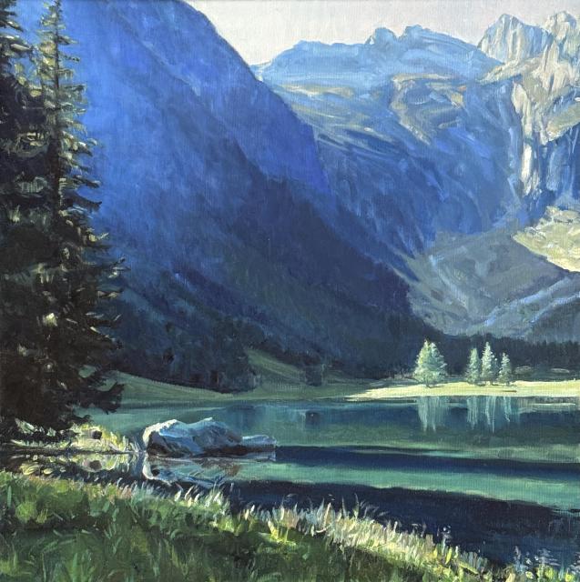 Ein spiegelglatter Bergsee von hohen Bergzinnen umgeben. Es ist Frühsommer, noch früh am Morgen und die ersten Sonnenstrahlen haben den See erreicht. 
Das Licht wirft noch lange Schatten, im smaragdblauen Wasser spielgen sich die Lärchen von der anderen Seite des Sees. Links, vom Bildrand abgeschnitten stehen dunkle Tannen. Diel Luft wirkt frisch und vom Licht durchdrungen.