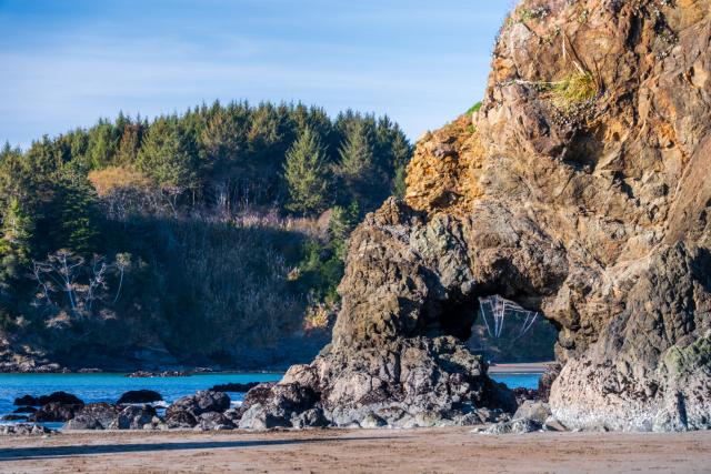 A stone arch on the beach, in front of a small island. [Fuji X-T5 / Fuji 35 1.4]