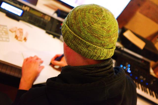 a person with a green beanie is writing something onto an envelope at a studio desk