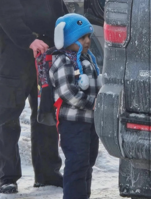 Photo of Liam Ramos in a blue hat and plaid jacket being put in a dark vehicle 