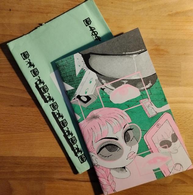 Grey, pink, and green cover of a zine with an illustration of a person on the street wearing glasses. The green envelope the zine arrived in is visible below the zine. 404 Media's logo and iconography are visible.