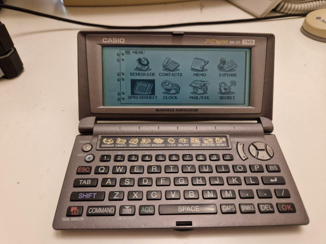 A photo of a tiny pocket organiser with a QWERTY keyboard, showing the main menu (calendar, scheduler, spreadsheet, etc) on its monochrome screen