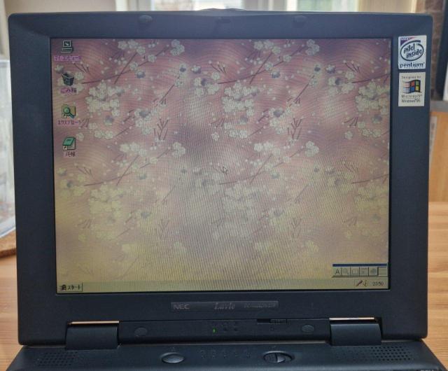 A photo of a NEC Lavie laptop screen with"Pentium Inside, Windows 95" stickers on the side. The desktop shows default sakura wallpaper