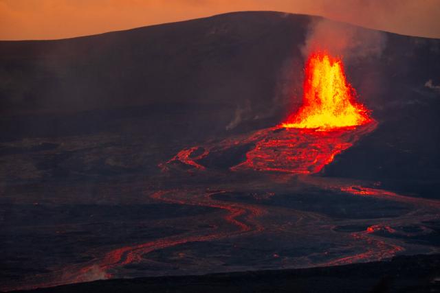 A volcano erupts amidst a dark rocky landscape, with its flow visibly running downhill. [Fuji X-T5 / Tamron 18-300]