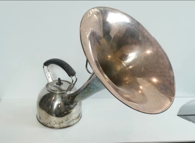 A standard metal tea kettle but the end has been modified into a very large horn like a tuba might have.