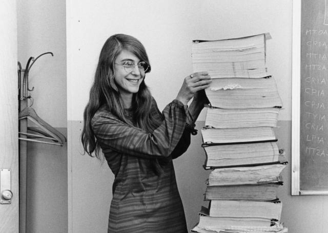 Margaret Hamilton, standing next to a huge stack of paper with the printout of the Apollo LEM code