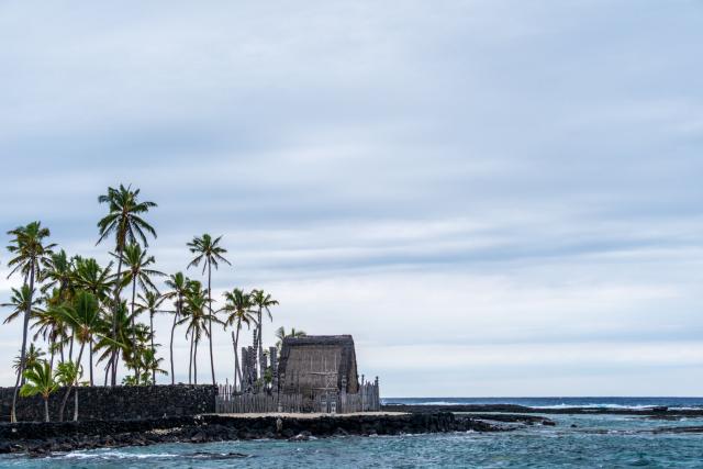 A building stands on a black rock promontory jutting into the sea, with palm trees around. [Fuji X-T5 / Tamron 18-300]