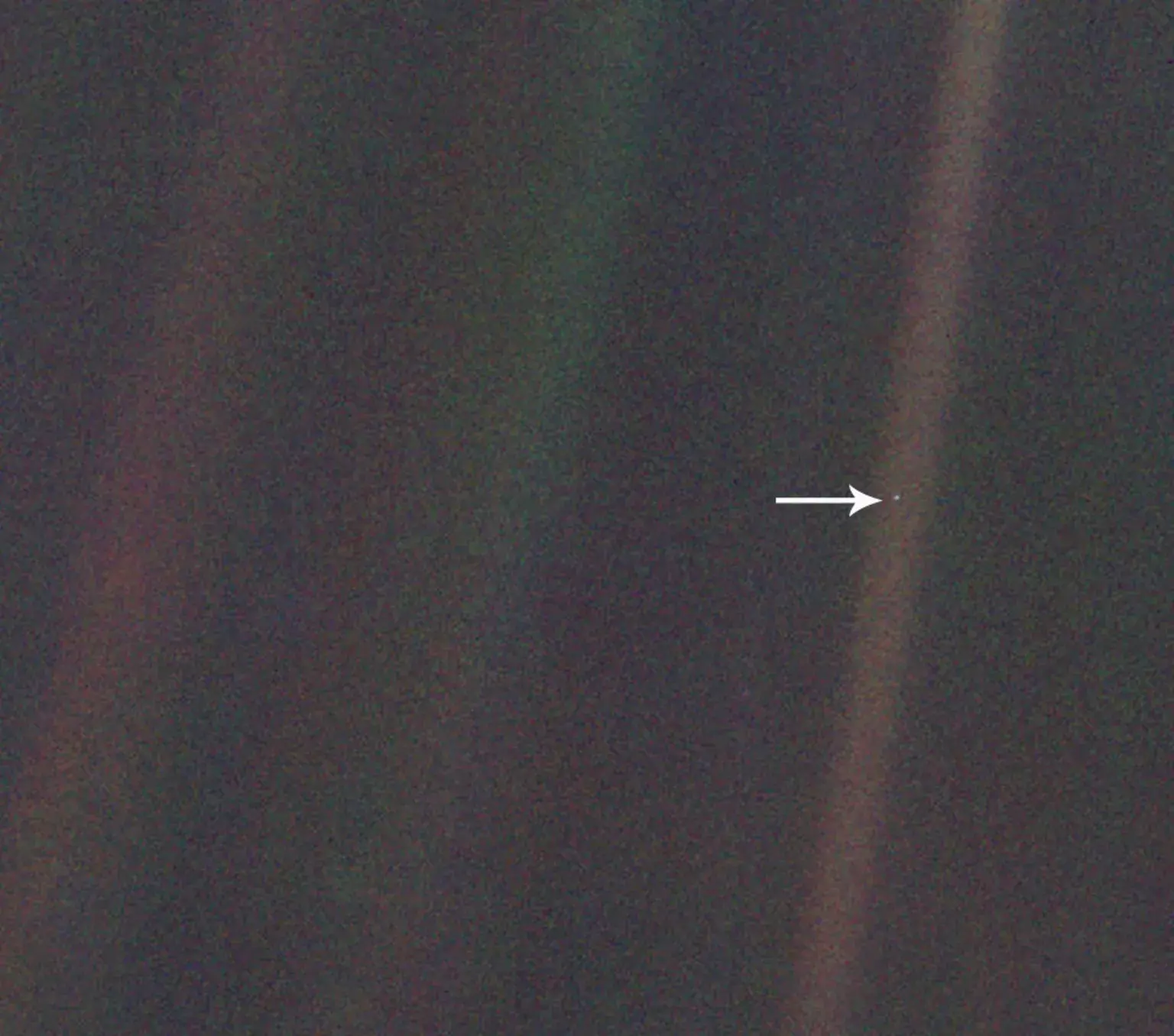A grainy, low resolution image of space, with faint bright-colored streaks. An arrow points to a small dot, our very own planet Earth.