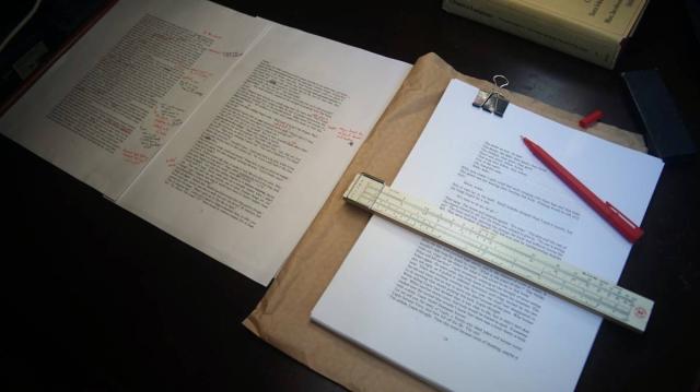 a photo showing handwritten corrections on a printed manuscript, with a slide rule used to make lines.
