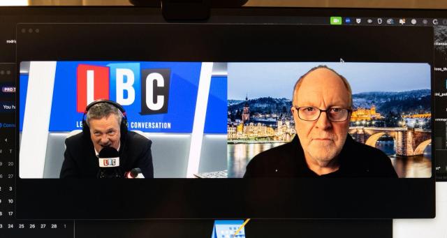 A photo of my monitor showing a Zoom conversation between me on the right and Matthew Wright, LBC presenter on the left. He has the LBC studio and logo behind him; I have a (virtual) picture of a snowy Heidelberg behind me. 