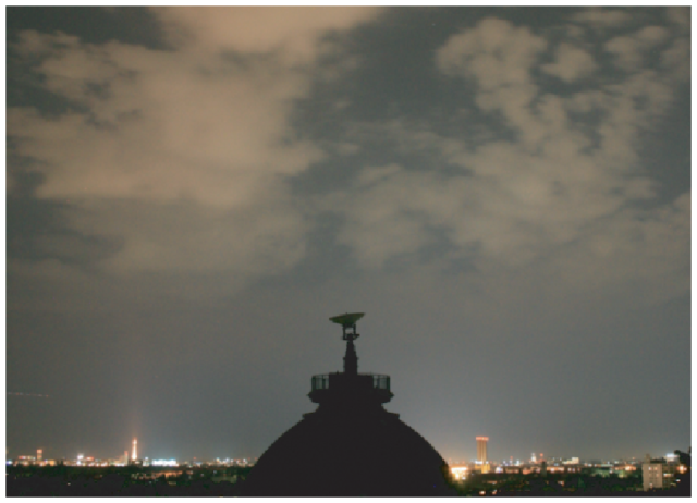 Image from the paper showing a cloudy urban sky, where the clouds brighten the sky. A building with a satellite dish on top is a dark silhouette. 
