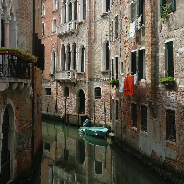 A backwater canal in Venice, with laundry, a boat, and a variety of windows and balconies.