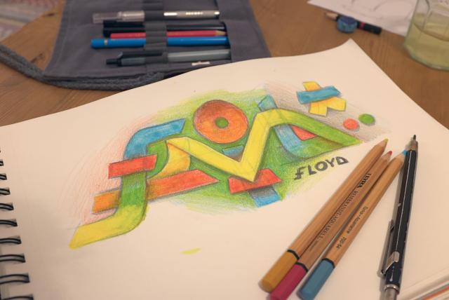 A sketch block on a wooden table. The sketch somehow spell the letters FLOYD in gradient colors of blue, red, green, yellow orange and purple.