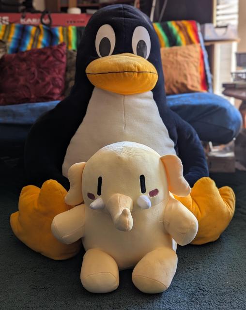 A stuffed elephant sits just in front of a large stuffed penguin.