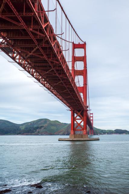 A large suspension bridge stretches across water to far-off land.  [Ricoh GR III]