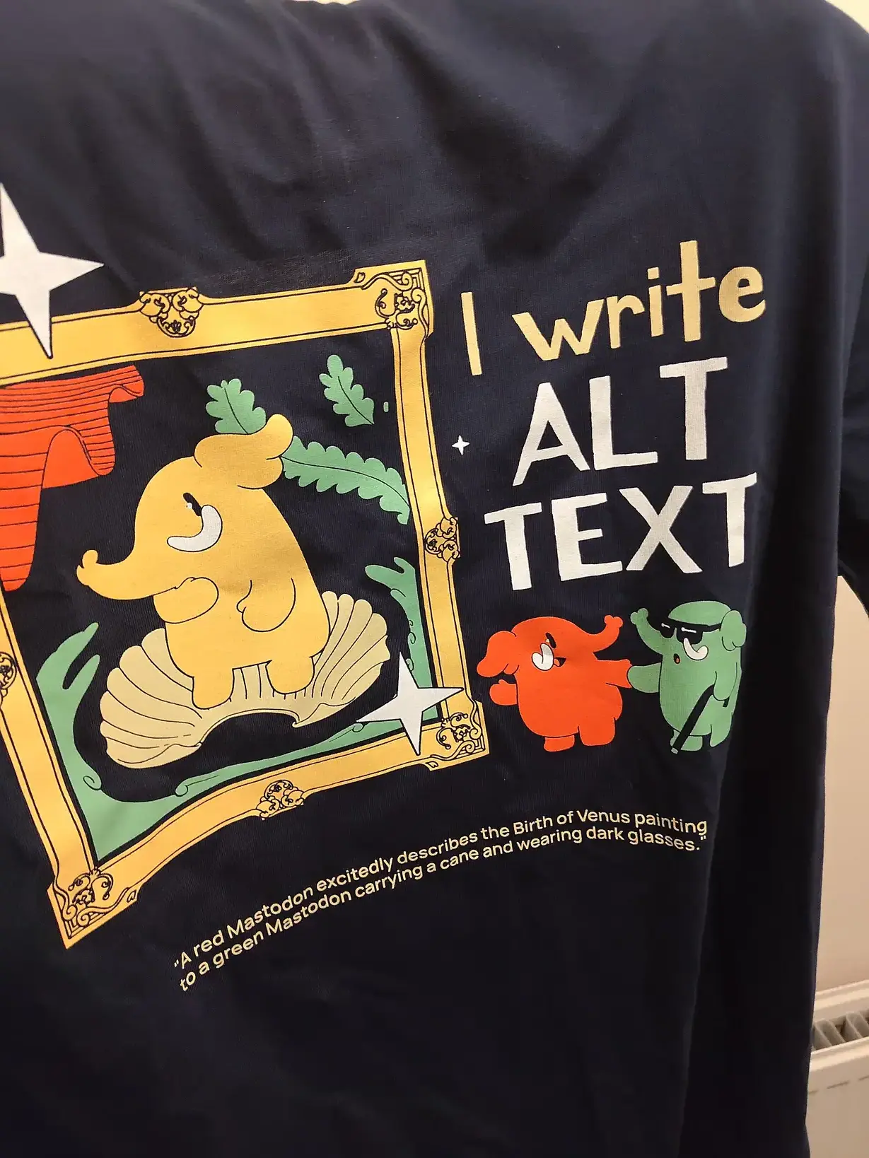 The Mastodon alt text shirt being held up by an arm running through its selves.