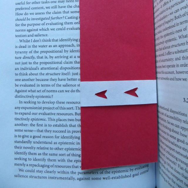 A strip of bright red card-stock with a white band around it. The band has two leftward-facing arrows cut out of it so the red shines through. It's lying in an open book with rather small text, and the band could be slid up or down to point at different parts.