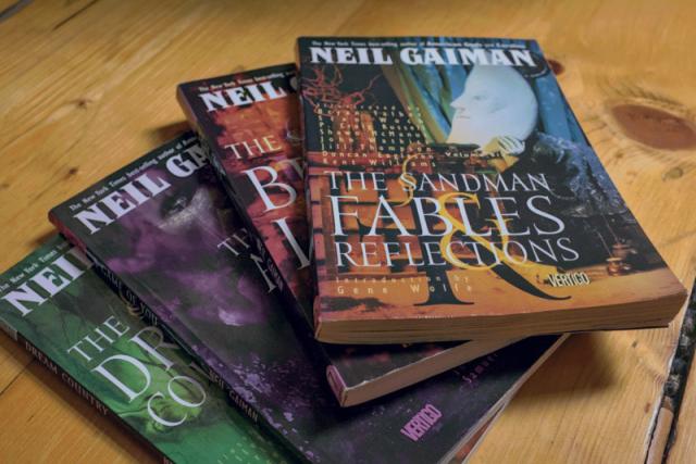 Four issues of The Sandman comics by Neil Gayman laying on a wooden floor.