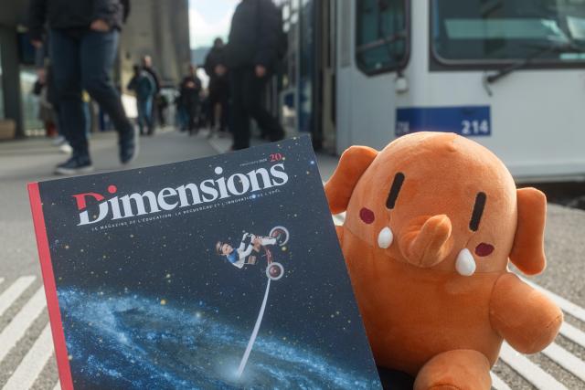 Plushtodon à la sortie du m1, à l'EPFL, tenant dans ses mains le vingtième numéro du magazine Dimensions. Sur la couverture, une illustration de Plonk&Replonk avec un enfant traversant une galaxie sur un tricycle