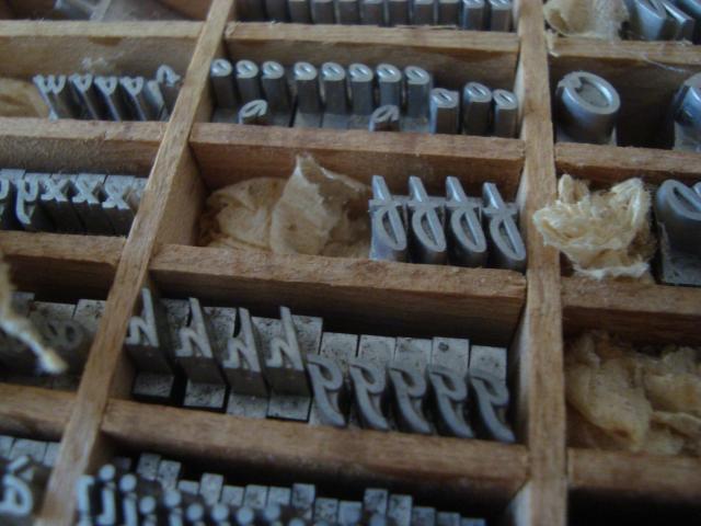 Photographie de caractères plomb dans une casse en bois. Lettres f, h, g dans une espèce de script un peu vintage.