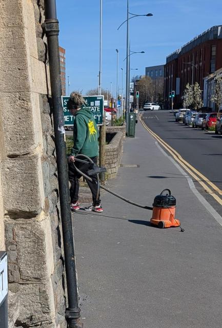 A man walking down the street pulling a Henry vacuum cleaner by the end of the hose 