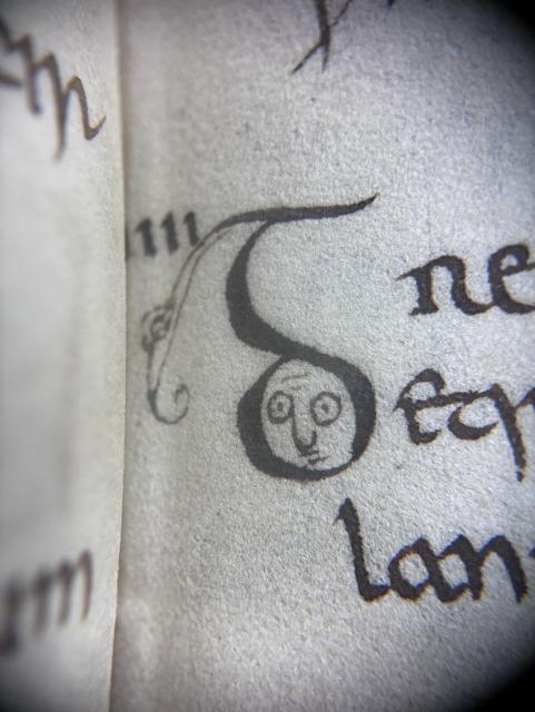 A close-up view of an old manuscript page featuring a stylized figure with a round face and large eyes, with handwritten text in an ornate script.
