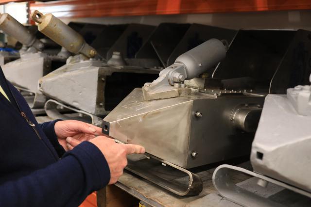 A pair of hands holding the front of a metal device that looks like a pyramid on its side, with a small opening in the front. This is a continuous plankton recorder.