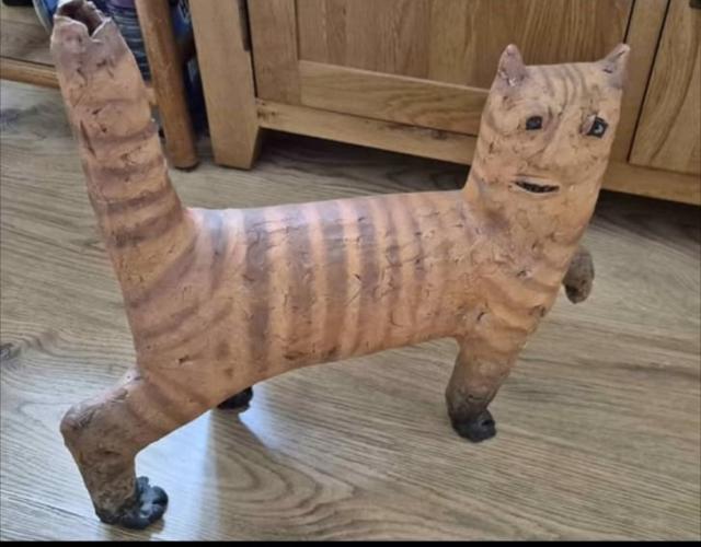 A clay statue of a cat. It had a human face for some reason, and the tail is very fat. Other than that it is very much a cat. It has ginger striped fur and dark paws.