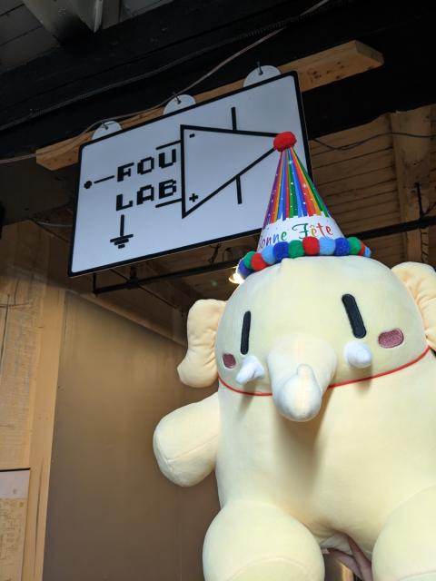 Mastodon plush wearing a HAPPY BIRTHDAY hat, raised above the foulab sign.