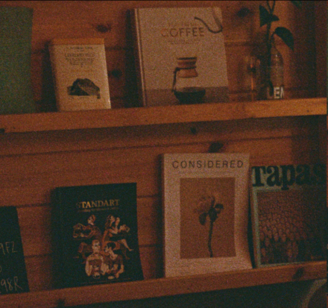 A shelf with books, the titles cannot be read very clearly except for the largest text on each, one says "Coffee", one says "Standard", another says "Considered" and the last one "Tapas".