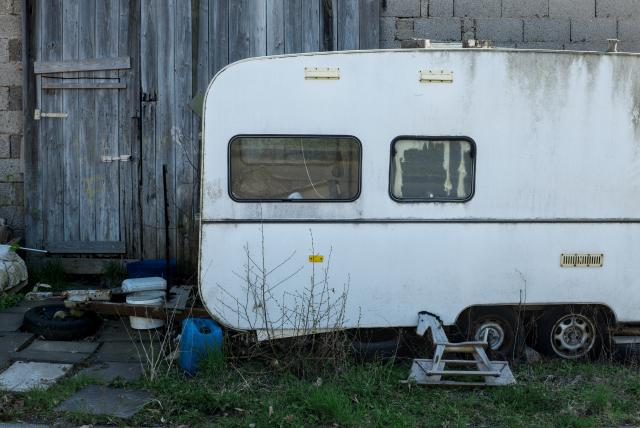 ein ausgemustertes schaukelpferd vor einem ausgemusterten wohnwagen
