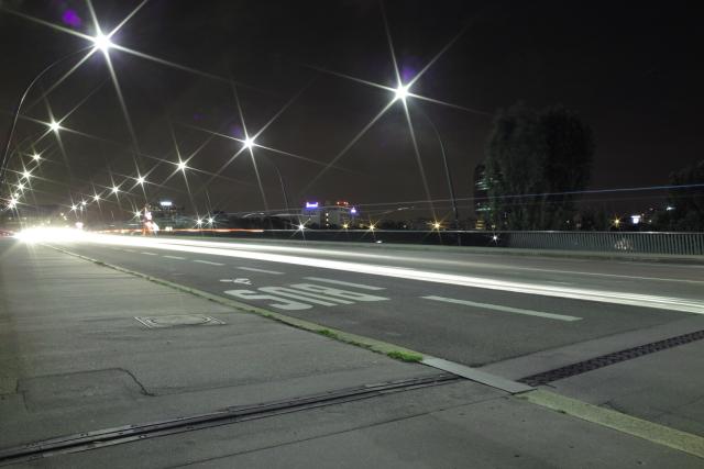 Une rue de nuit, une voiture passe et laisse une traînée lumineuse les lampadaire forme des étoiles