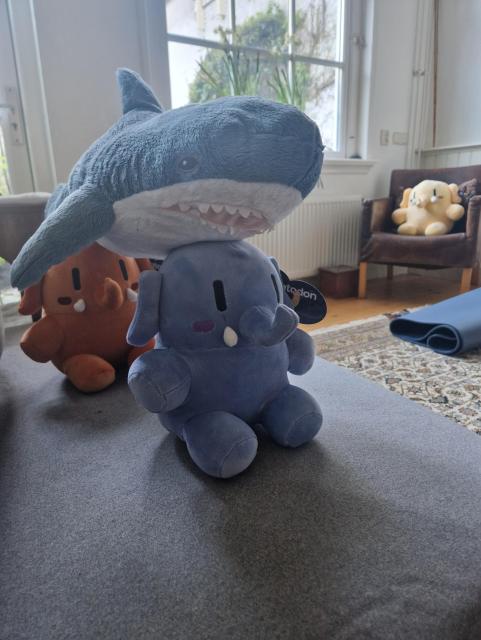 Blue and red mini mastodonts with a blåhaj on their heads. In the distance the big yellow masto is looking on in awe.