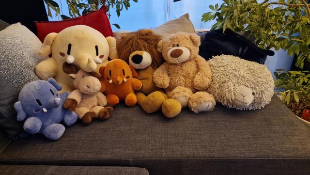 From left to right: blue #plushtodon, yellow big #plushtodon, elk, orange #plushtodon, lion, teddy & sheep.

All of them stuffed animals / plushies, sitting on the couch together like a big happy chosen family.